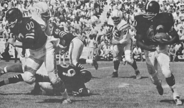 The Oakland Raiders sporting their black uniforms in 1962. Legendary All-AFL Center Jim Otto (#00) leads the way for runner Bo Roberson (#40). Other Raiders pictured are longtime lineman Wayne Hawkins (#65) and Dan Ficca (#69). The tangled-up Charger is none other than the great Ernie Ladd (#77).