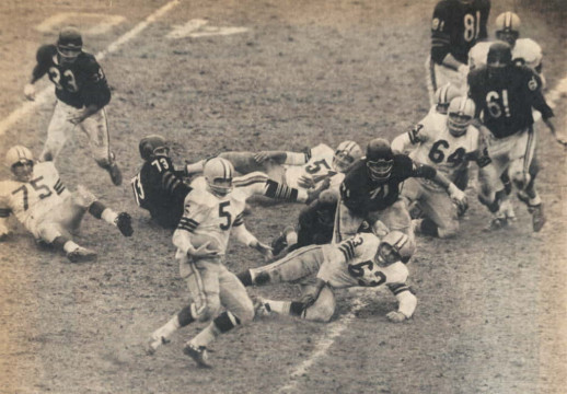 NFL action from, we think 1960. Packers great Paul Hornung carries against the Chicago Bears defense. Those players identifiable in the picture are some of the best known players in the league at the time. 
For Green Bay we have All Pro Forrest Gregg (#75), All Pro Paul Hornung (#5), All Pro Jim Ringo (#51), Fuzzy Thurston (#63) and All Pro Jerry Kramer (#64). For the Bears defense - Larry Morris (#33), Bill Bishop (#73), Earl Leggett (#71), Pro Bowler Doug Atkins (#81) and All Pro Bill George (#61).
