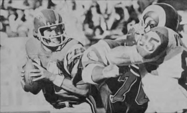 Dan Fouts (#14) gets behind the blocking of tackle Russ Washington (#70) as Ram defender Jack Youngblood (#85) powers in. From the 1975 contest between LA and San Diego, the Rams would pull out a 13-10 overtime win. 