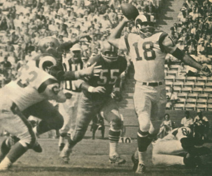 In 1964 Rams QB Roman Gabriel (#18) was making a name for himself as one of the strongest quarterbacks in the NFL. Here Rams lineman Joe Carollo (#63) works to keep 49ers away while longtime San Francisco linebacker Matt Hazeltine (#55)e moves in.  