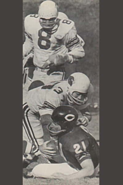 Black and white photo depicting Jon Arnett on the ground, being stopped by Cardinals players Pat Fisher and Larry Wilson.