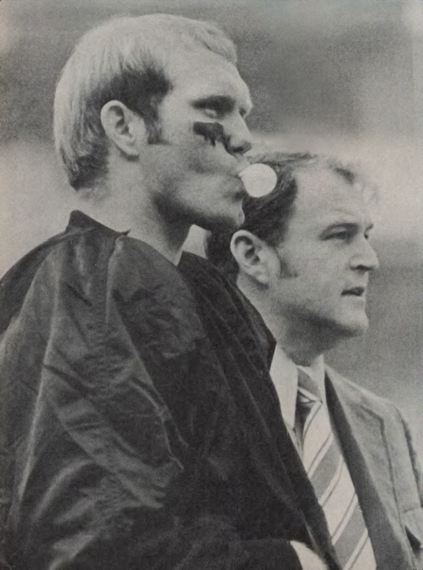 a picture of a young Terry Bradshaw chewing gum on the sideline next to head coach Chuck Noll.