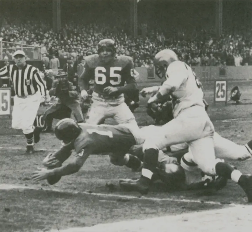 Black and white photo of Frank Gifford scoring against the Redskins in 1956.