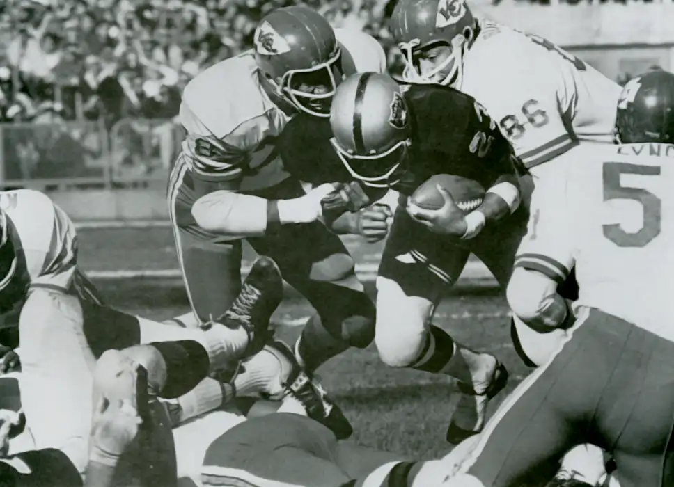 Raiders running back Charlie Smith is stopped by Chiefs defenders Bobby Bell and Buck Buchanan during the 1969 AFL Championship Game. Despite scoring Oakland's only touchdown, Smith was limited to just 31 rushing yards as Kansas City's dominant defense recorded four sacks and four interceptions in a 17-7 victory that sent the Chiefs to Super Bowl IV to face the NFL champion Minnesota Vikings.